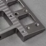 Close up of a brushed titanium alloy metal bracket with threaded holes